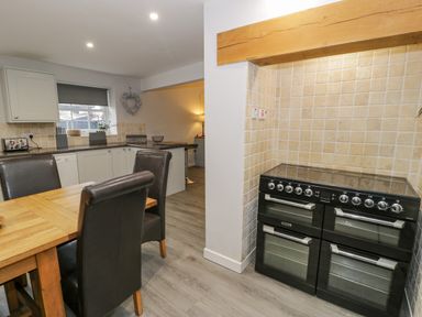 A kitchen with a black double oven a wooden dining table with four chairs and white cabinets at Bodrual Cottage in Rhosbodrual near Caernarfon