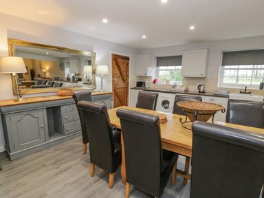 A kitchen with a wooden dining table and black chairs and a large mirror on the wall at Bodrual Cottage in Rhosbodrual near Caernarfon