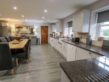 A kitchen with a long dining table and black chairs next to white cabinets and gray countertops at Bodrual Cottage in Rhosbodrual near Caernarfon