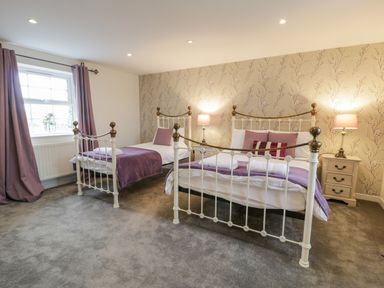 A bedroom with two white metal beds purple blankets and pillows floral wallpaper and bedside tables with lamps at Bodrual Cottage in Rhosbodrual near Caernarfon