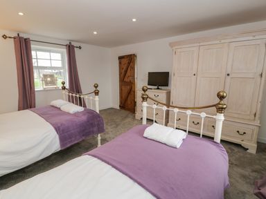A bedroom with two single beds covered with purple blankets and white towels a wooden wardrobe a dresser with a television and a window with purple curtains at Bodrual Cottage in Rhosbodrual near Caernarfon