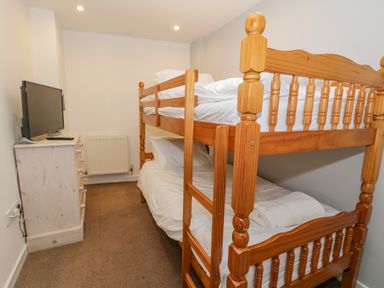 A small bedroom with a wooden bunk bed a chest of drawers with a television on top and a radiator on the wall at Bodrual Cottage in Rhosbodrual near Caernarfon