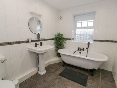 A bathroom with a freestanding bathtub a pedestal sink a round mirror and a potted plant at Bodrual Cottage in Rhosbodrual near Caernarfon