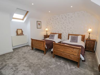 A bedroom with two wooden single beds bedside tables lamps and a skylight window at Bodrual Cottage in Rhosbodrual near Caernarfon