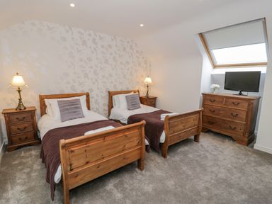 A bedroom with two single beds lamps on bedside tables a dresser with a television and a window at Bodrual Cottage in Rhosbodrual near Caernarfon