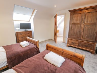 A bedroom with two single beds with brown blankets and white towels wooden furniture a chest of drawers with a TV and a wardrobe at Bodrual Cottage in Rhosbodrual near Caernarfon