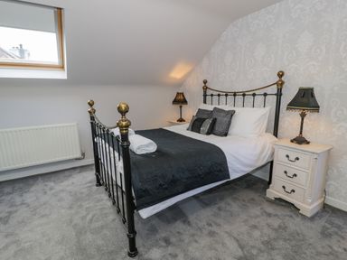 A bedroom with a metal bed frame, bedside tables with lamps, gray carpet, and a skylight window at Bodrual Cottage in Rhosbodrual near Caernarfon