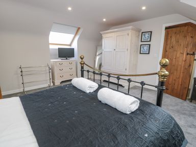 A bedroom with a black metal bed, two rolled towels, a white chest of drawers with a TV, a white wardrobe, a wooden door, and a skylight window at Bodrual Cottage in Rhosbodrual near Caernarfon