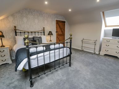A bedroom with a metal bed frame a wooden door two bedside tables with lamps a dresser with a television and a towel rack at Bodrual Cottage in Rhosbodrual near Caernarfon