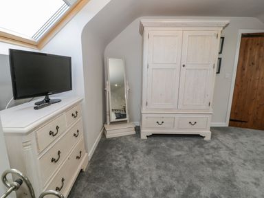 A bedroom corner with a white dresser holding a TV a standing mirror and a white wardrobe on a grey carpet at Bodrual Cottage Rhosbodrual near Caernarfon