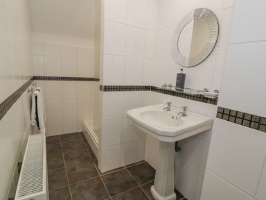 A bathroom with a pedestal sink mirror soap dispenser and a shower area at Bodrual Cottage in Rhosbodrual near Caernarfon