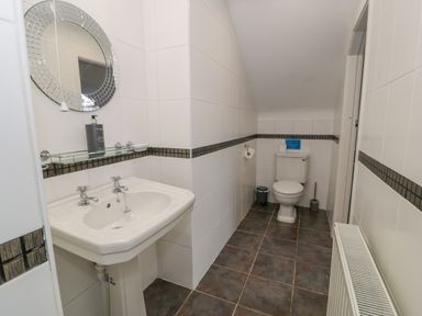 A bathroom with a sink a round mirror a toilet and tiled walls at Bodrual Cottage in Rhosbodrual near Caernarfon