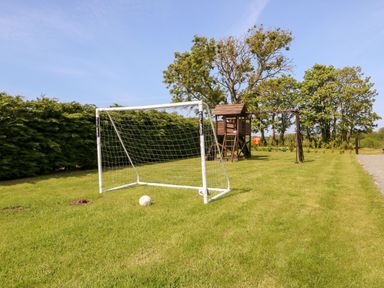 A garden with a soccer goal and ball and a wooden playhouse with swings at Bodrual Cottage in Rhosbodrual near Caernarfon