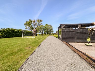A gravel pathway between a grass field with a soccer goal and wooden playhouse and a covered wooden structure at Bodrual Cottage in Rhosbodrual near Caernarfon