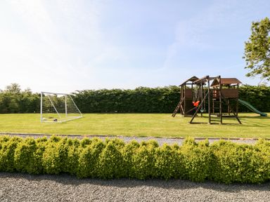 A garden with a soccer goal and balls and a wooden playset with swings and a slide at Bodrual Cottage in Rhosbodrual near Caernarfon