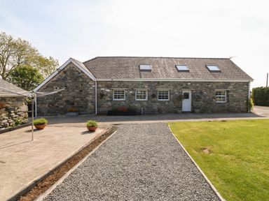 A stone cottage with a gravel path and grass lawn at Bodrual Cottage in Rhosbodrual near Caernarfon
