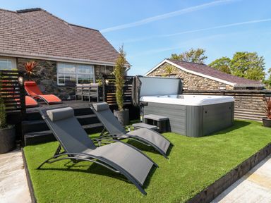 A backyard with two gray lounge chairs a hot tub and a raised deck with orange lounge chairs at Bodrual Cottage Rhosbodrual near Caernarfon
