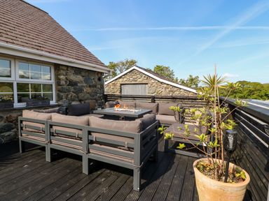An outdoor seating area with a sectional sofa and fire table on a deck at Bodrual Cottage in Rhosbodrual near Caernarfon