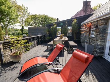 An outdoor deck with two red lounge chairs a wooden table with benches and plants in pots at Bodrual Cottage Rhosbodrual near Caernarfon