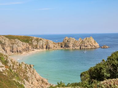 A rocky coastline with a sandy beach and a boat on the water at Beachcomber in Porthcurno near Sennen