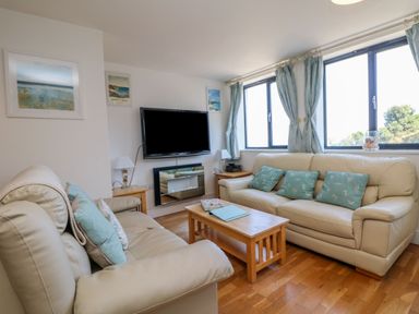 A living room with two beige sofas and blue cushions with a wooden coffee table and a wall-mounted TV at Beachcomber in Porthcurno near Sennen