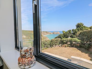 A glass vase filled with seashells on a windowsill overlooking a garden and a coastal bay at Beachcomber in Porthcurno near Sennen