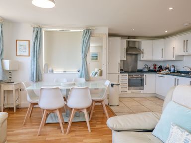 A kitchen and dining area with a glass table and white chairs at Beachcomber in Porthcurno near Sennen