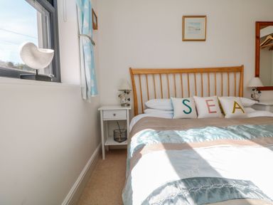 A bedroom with a bed with SEA pillows bedside tables lamps a window with nautical curtains and a shell decoration at Beachcomber in Porthcurno near Sennen