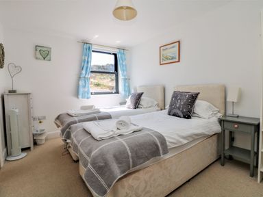 A bedroom with two single beds bedside tables and a window with blue curtains at Beachcomber in Porthcurno near Sennen