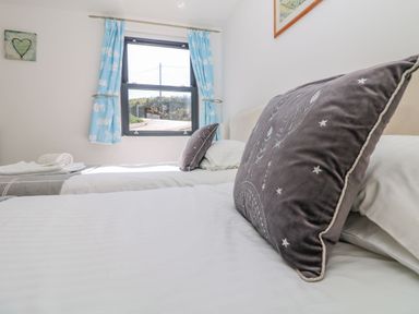 A bedroom with two beds white linens gray pillows and a window with blue curtains at Beachcomber in Porthcurno near Sennen
