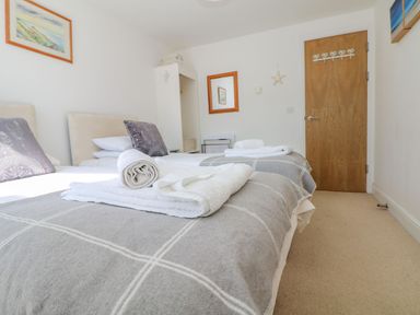 A bedroom with two single beds and folded towels on the beds at Beachcomber in Porthcurno near Sennen