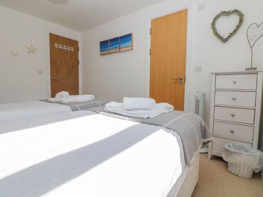 A bedroom with two beds and towels on them a chest of drawers and two wooden doors at Beachcomber in Porthcurno near Sennen