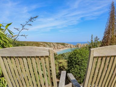 A wooden bench overlooking a coastal beach and rocky cliffs at Beachcomber in Porthcurno near Sennen