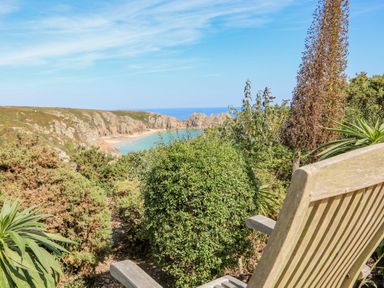 A wooden chair overlooking bushes with a view of a beach and rocky coastline at Beachcomber in Porthcurno near Sennen