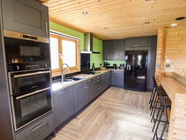 A kitchen with gray cabinetry black appliances wooden ceiling and floor and green walls at iLodge Ultra in Kenwick near Louth