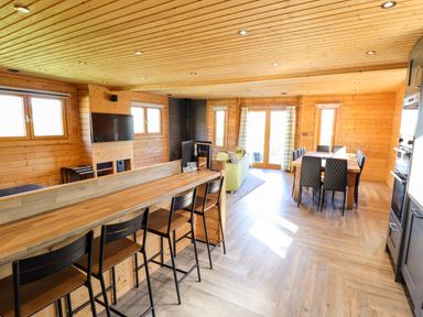 An open plan wooden interior with a kitchen counter with four stools a dining table with six chairs a green sofa and a wall mounted television at iLodge Ultra Kenwick near Louth
