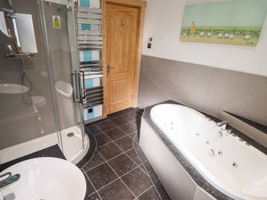 A bathroom with a bathtub shower cubicle washbasin and a wooden door at iLodge Ultra Kenwick near Louth