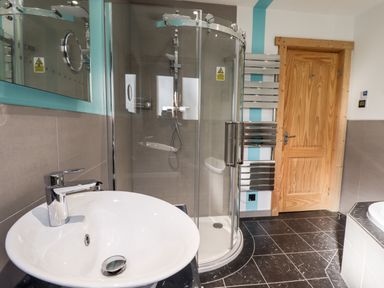 A bathroom with a white sink a glass shower cubicle a wooden door and a wall-mounted towel radiator at iLodge Ultra Kenwick near Louth