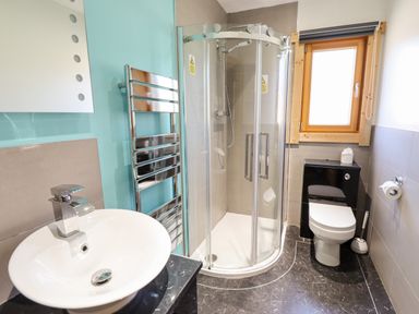 A bathroom with a round white sink a metal towel rack a corner glass shower and a toilet near a window at iLodge Ultra Kenwick near Louth