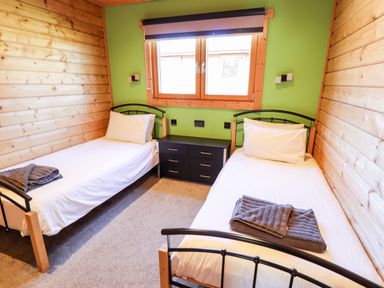 A bedroom with two single beds a black dresser under a window with green walls and wooden paneling at iLodge Ultra Kenwick near Louth