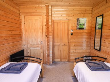 A bedroom with two single beds with blankets folded on them wooden walls a wooden door a closet and a mirror at iLodge Ultra Kenwick near Louth