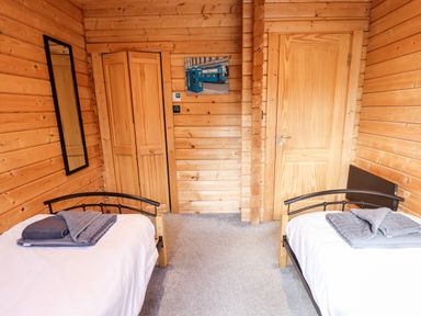 A wooden bedroom with two single beds towels on the beds a mirror on the wall and two wooden doors at iLodge Ultra Kenwick near Louth