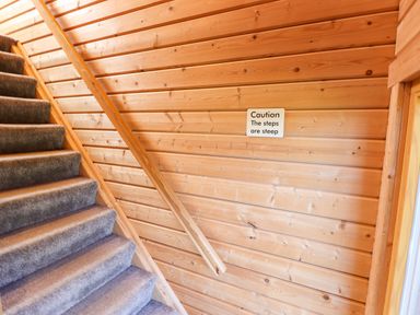 A carpeted staircase with wooden walls and a handrail with a caution sign at iLodge Ultra Kenwick near Louth