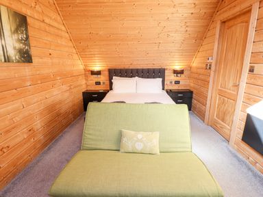 A bedroom with a green bench in front of a bed with white pillows and wooden walls at iLodge Ultra Kenwick near Louth