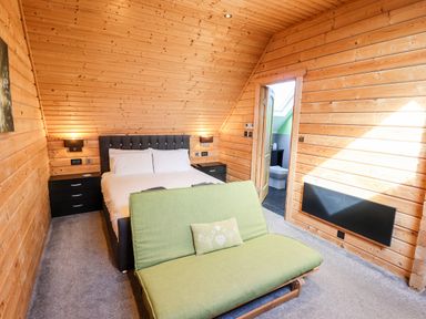 A bedroom with a double bed two black nightstands a green sofa and a door leading to a bathroom at iLodge Ultra Kenwick near Louth