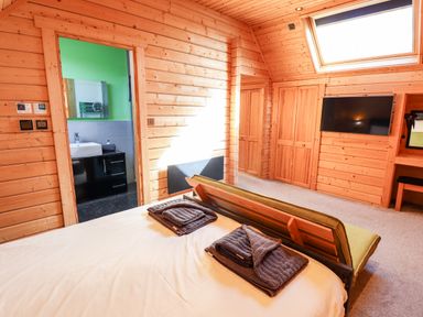 A bedroom with wooden walls a bed with folded towels a television and a window at iLodge Ultra Kenwick near Louth