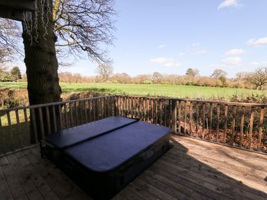 An outdoor wooden deck with a covered hot tub and a wooden railing overlooking a grassy field and trees at iLodge Ultra in Kenwick near Louth