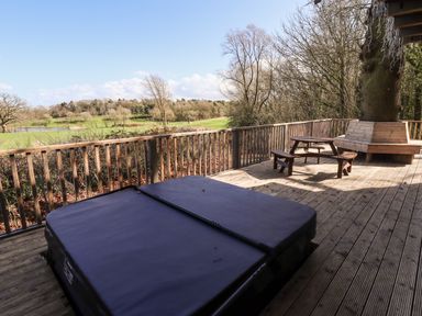 A wooden deck with a covered hot tub a round picnic table and a tree bench overlooking a park at iLodge Ultra Kenwick near Louth