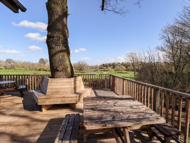 A wooden outdoor deck with built in bench around a tree and wooden picnic tables at iLodge Ultra Kenwick near Louth