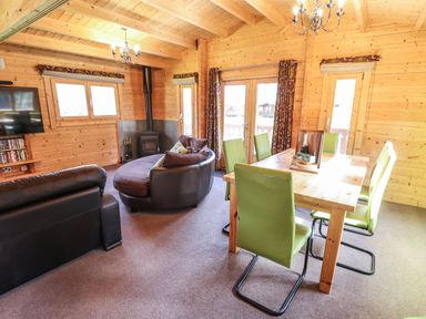 A living and dining area with green chairs a wooden table a round sofa a black stove and a television at iLodge 73 Kenwick near Louth